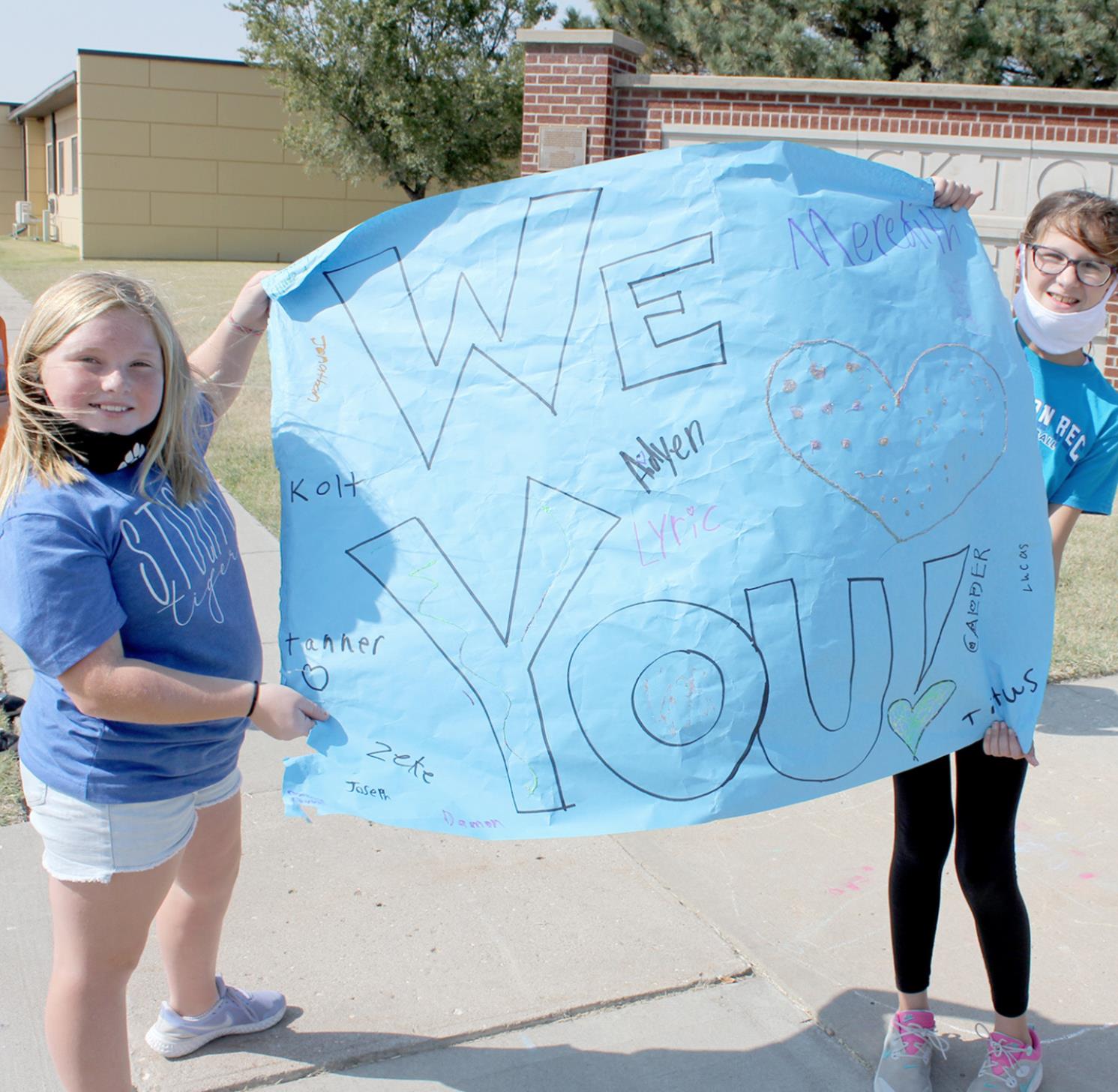 CLASSMATES AIDYN KERR (left) AND MEREDITH GASPER fight the wind as they display a “WE LOVE YOU” poster, signed by the fifth-grade class.