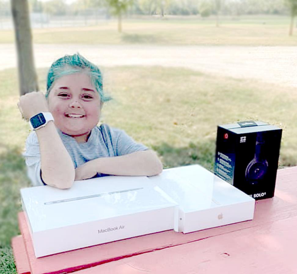 WISHES GRANTED! Serenity rests at a picnic table in the City Park, and happily displays her gifts: iWatch, MacBook Air, iPad, and Beats headphones. These gifts will all help Serenity stay in touch with her friends and family as well as keep up with school work.