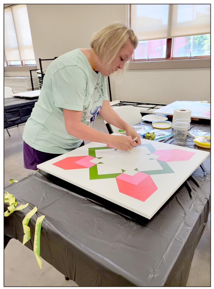 CRYSTAL STAPLETON carefully masks the next area to be painted on a colorful Barn Quilt. When finished, this will be one of the “greeting” blocks.