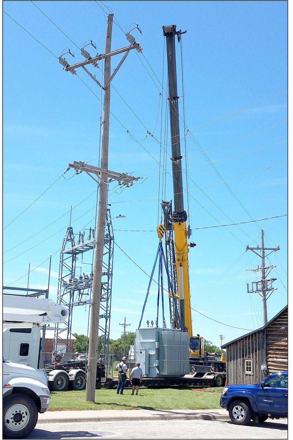 WITH SLINGS ATTACHED, the huge Hess crane lifts the faulty transformer off of its base to make way for the replacement.