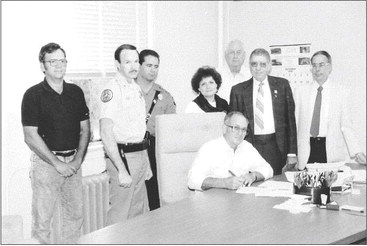 PRIOR TO THE WEEKLY MEETING of the Rooks County Commissioners, chairman Gene Jaco signed a proclamation making October 1990 Alcohol and Other Drugs Awareness Month. Those present for the signing were (from left): commissioner Charles Allphin, sheriff Dave Denton, highway patrol trooper Mark Bacon, magistrate judge Nancy Conyac, commissioner Robert Stice, outreach consultant Tommy D. Tomlin, and county attorney Leonard J. Dix. Commissioner Gene Jaco is seated at the table.