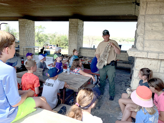 GAME WARDEN JAKE BROOKE talked about wildlife identification using skins of the animals to the many boys and girls that attended the Outdoor Adventure Day at Rooks State Fishing Lake on Tuesday, June 6th.