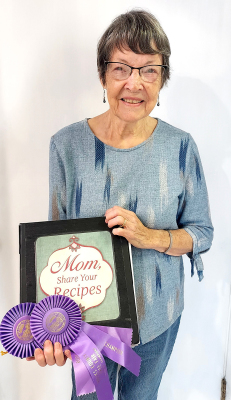 JEAN LINDSEY has entered items from flowers to collages at the Rooks County Free Fair for the past 80 years. She is pictured with some ribbons and the recipe book, a Grand Champion winner she made for her family as a Christmas present in 2013.
