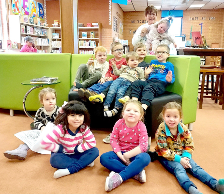 THE FRIDAY STORYTIME KIDS tested out the new furniture by posing for a picture! They are (sitting from left): Brooklyn Brass, Kamia Galloway, Grace Towne, Alena Riffel; (sitting on the couch) Fin Larson, Jasper Miller, Sully Larson, Ned Berkley, Jax Miller; (standing behind the couch) librarian Chris Sander holding Bailey Brass.