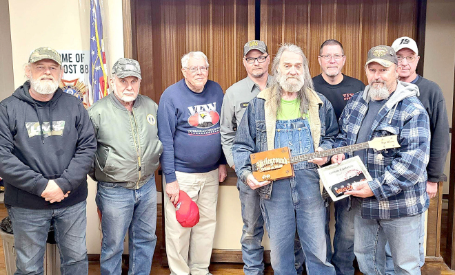 ROYCE WILLIAMS with Royce’s CBG donated one of his cigar box guitars to the Stockton VFW and American Legion to use as a raffle fundraiser for their organization. Pictured accepting the guitar are (from left): Scott Baker, Ken Bachman, John Berkley, Shayn Balthazor, Royce Williams, Mack Palmer and Ed Thayer.